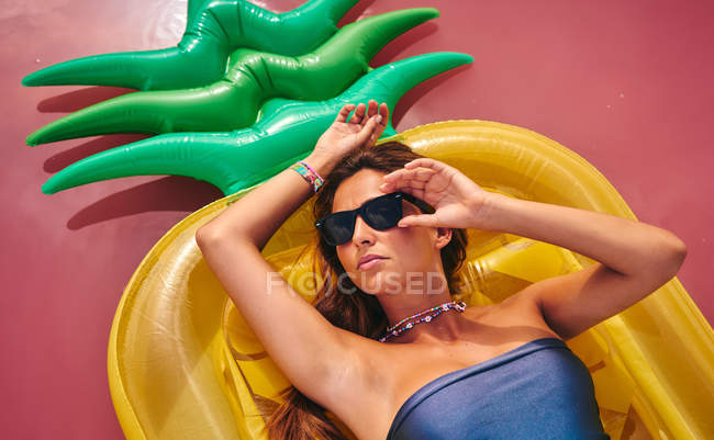 Мрійлива красива жінка в сонцезахисних окулярах відпочиває на надувному матраці — стокове фото