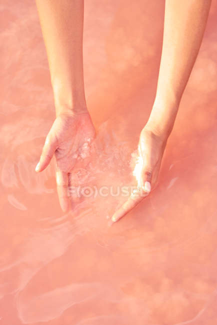 Mãos femininas tocando pilha de sal de cura em água rosa — Fotografia de Stock