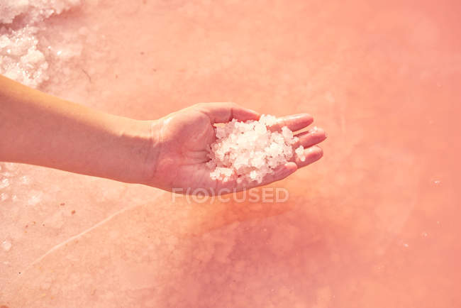 Mão feminina segurando pilha de sal de cura em água rosa — Fotografia de Stock