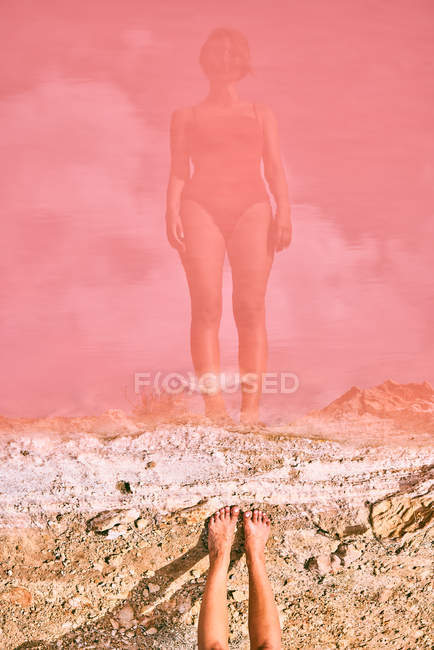 Reflecting in water of fit woman in swimsuit posturing on pink lake shore — Stock Photo