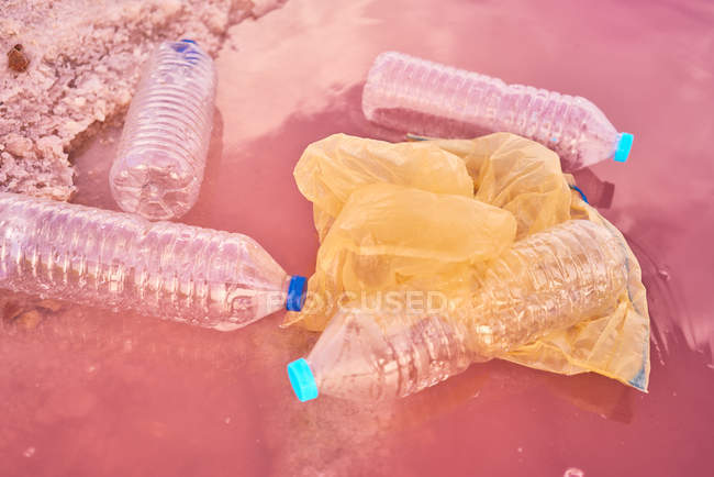 Plastic bottles and bags floating near shore at red lagoon with pink salty water — Stock Photo
