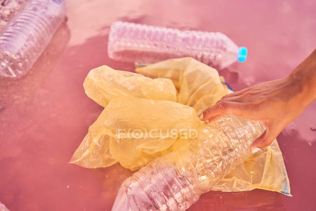 Nahaufnahme einer Hand, die Plastikmüll im verschmutzten Meerwasser berührt — Stockfoto