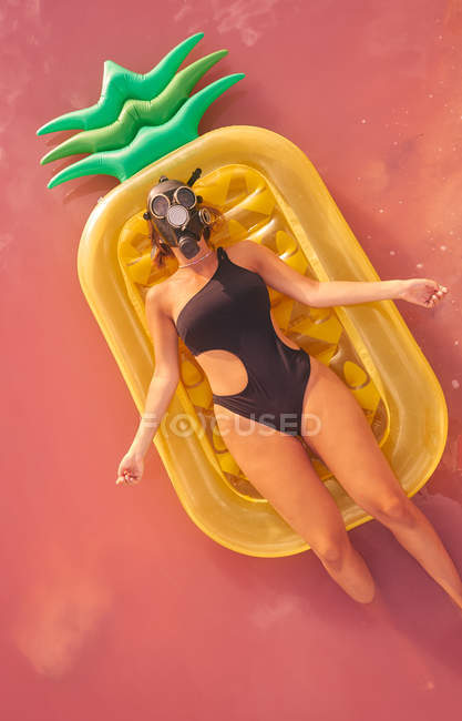 Dall'alto donna in maschera respiratore e costumi da bagno agghiacciante su materasso gonfiabile in forma di ananas in acqua laguna rossa — Foto stock
