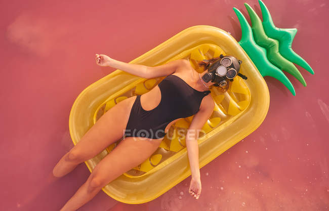 Donna in maschera respiratore sdraiata su materasso ad aria in acqua di lago rosa — Foto stock