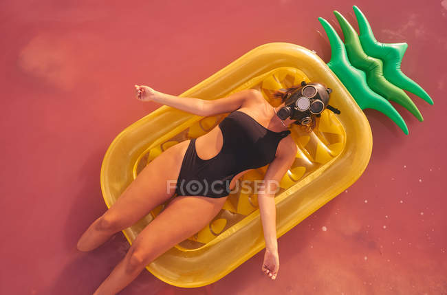 Mulher na máscara respirador deitado no colchão de ar na água do lago rosa — Fotografia de Stock