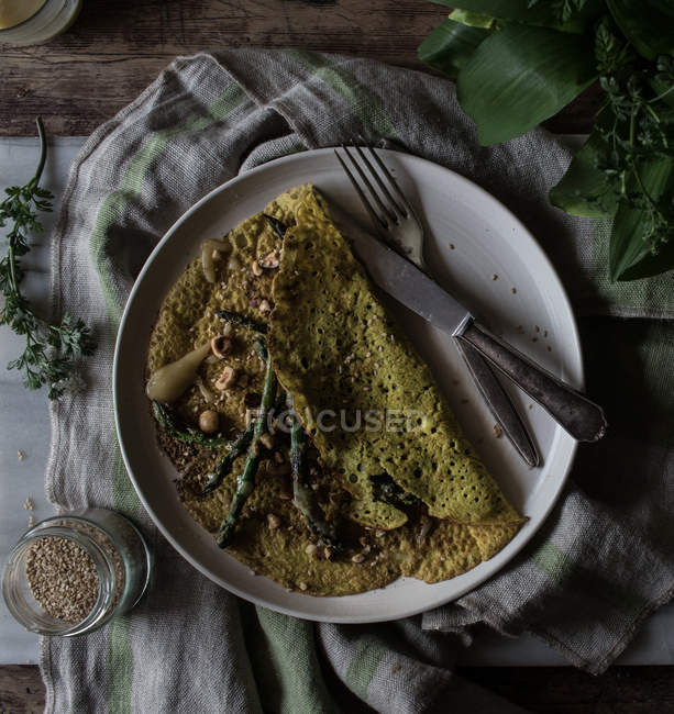 Oat crepe with asparagus and tahini paste served on white plate on rustic background — Stock Photo