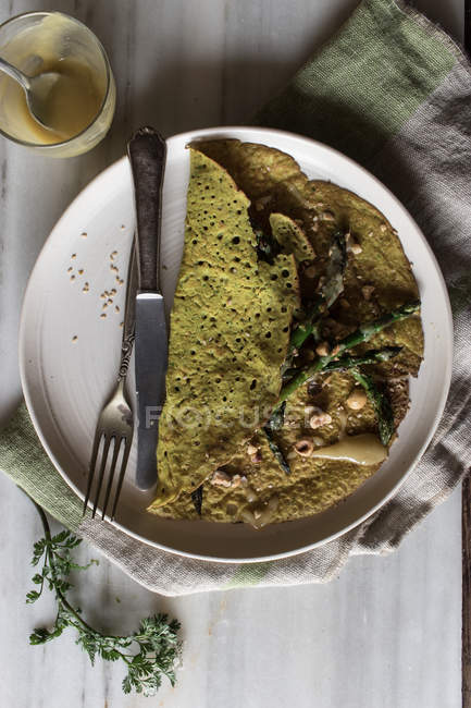 Oat crepe with asparagus and tahini paste served on white plate on rustic background — Stock Photo