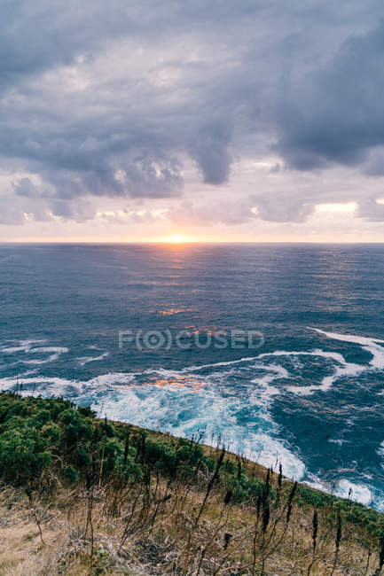Coast with dry grass near stormy sea in cloudy evening during beautiful sunset — Stock Photo