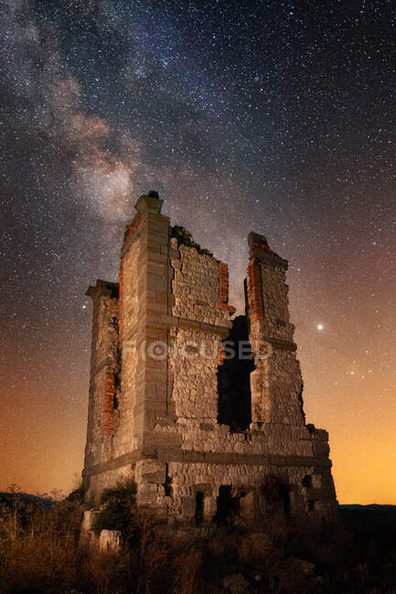 Ancienne tour de briques dilatée sur un champ désert contre un ciel étoilé majestueux — Photo de stock