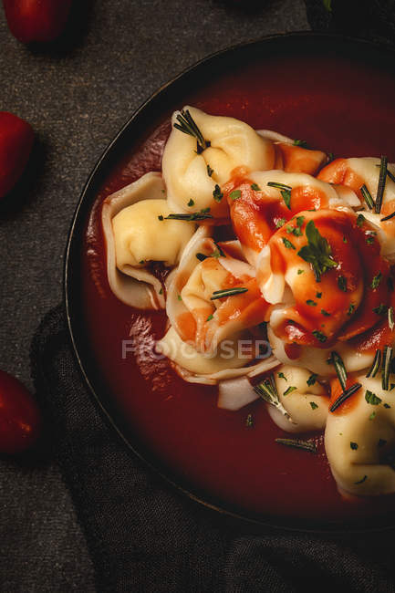 Cooked ravioli with tomato sauce and herbs in bowl next to fork and napkin on table — Stock Photo
