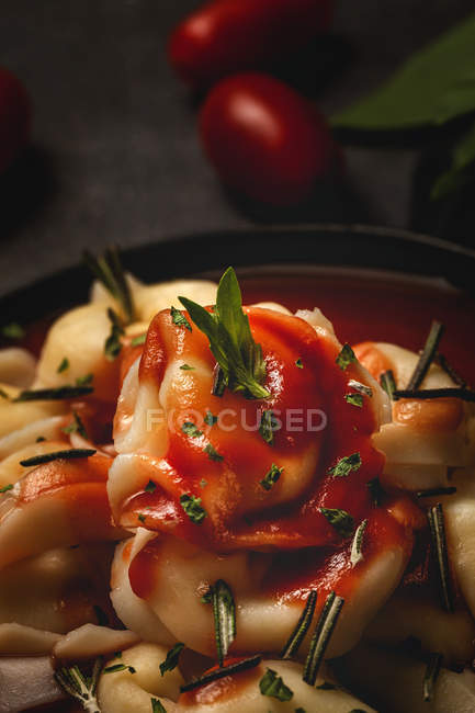 Raviolis cuits avec sauce tomate et herbes dans un bol à côté de la fourchette et serviette sur la table — Photo de stock