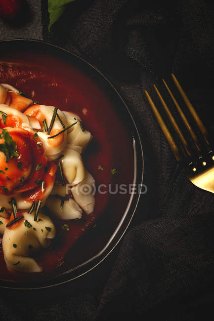 Ravioli cozido com molho de tomate e ervas na tigela ao lado de garfo e guardanapo na mesa — Fotografia de Stock
