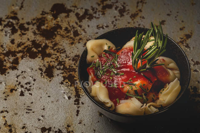 Cooked ravioli with tomato sauce and herbs in bowl next to fork and napkin on table — Stock Photo