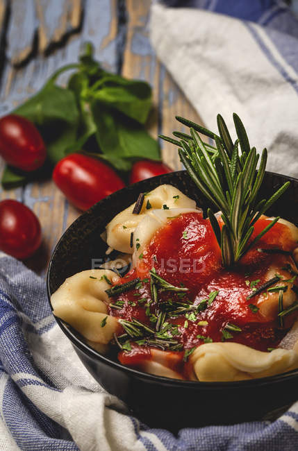 Ravioli cotti con salsa di pomodoro ed erbe aromatiche sul piatto accanto ai pomodori e stoffa sul tavolo rustico in legno — Foto stock