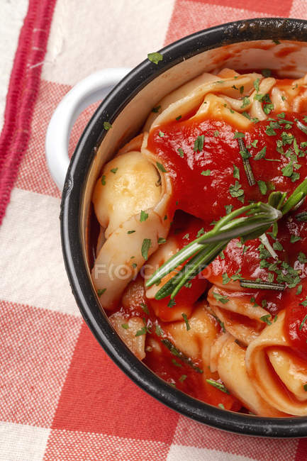 Cooked ravioli with tomato sauce and herbs on sauce pan casserole next to tomatoes on cloth in a table — Stock Photo