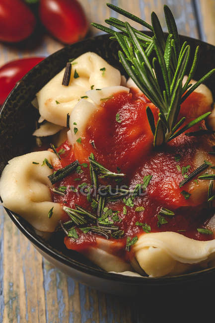 Gekochte Ravioli mit Tomatensauce und Kräutern in Schüssel neben Gabel und Serviette auf dem Tisch — Stockfoto
