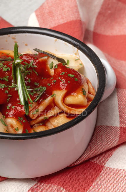 Raviolis cocidos con salsa de tomate y hierbas en cazuela de salsa junto a tomates sobre tela en una mesa - foto de stock