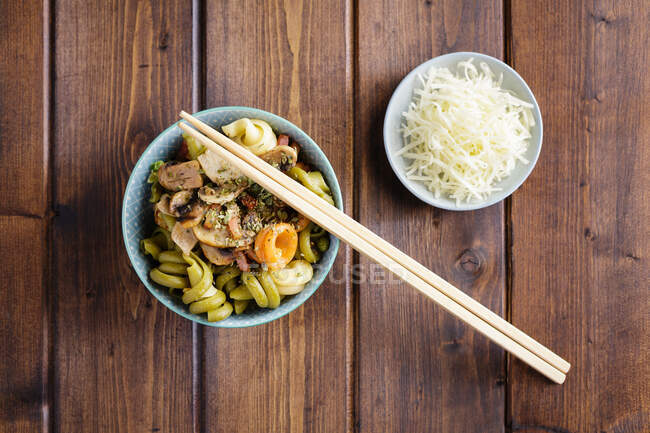 Органические макароны с овощами в миске и суши палочки на деревянном столе с миской гарнира — стоковое фото