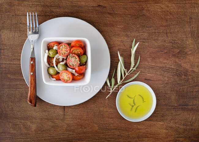 From above composition of salad with cherry tomatoes and olives in bowl and oil on side served on shabby wooden background — Stock Photo