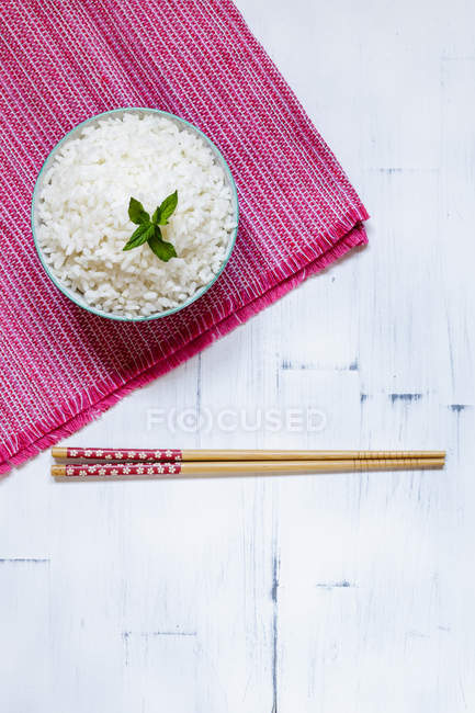 Bowl of traditional Japanese rice on pink towel and chopsticks on white table. — Stock Photo