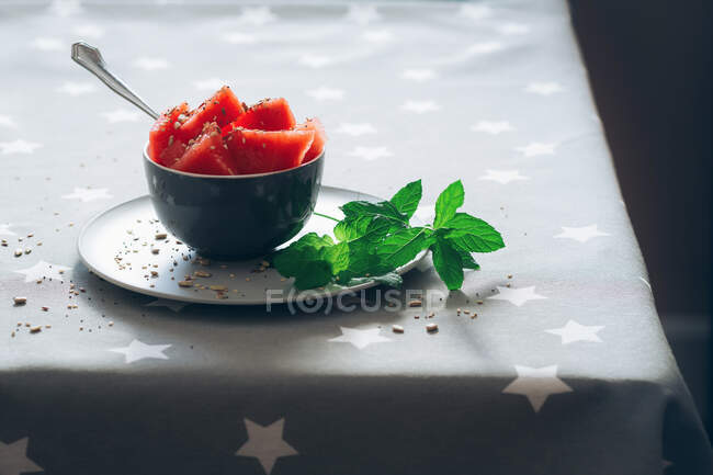 Cut pieces of watermelon in bowl garnished with mint leaves and corn on tablecloth — Stock Photo