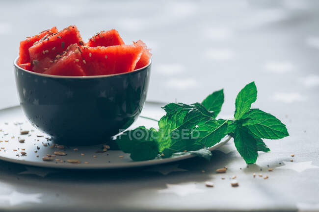 Cut pieces of watermelon in bowl garnished with mint leaves and corn on tablecloth — Stock Photo