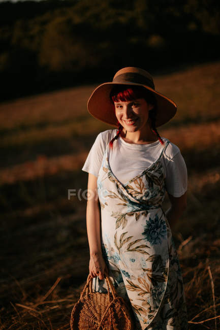 Frau in Retro-Kleid und Hut läuft im Feld dem Sonnenuntergang entgegen, während sie in die Kamera blickt — Stockfoto