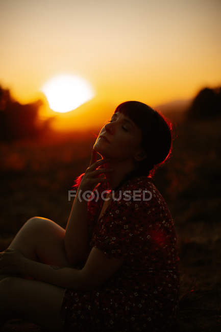 Vista laterale della donna sensuale fingendo di toccare il sole tramonto luminoso in cielo serale in campagna — Foto stock