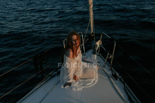 Relaxed beautiful woman sitting on bow of ship and resting while enjoying sea trip with closed eyes — Stock Photo