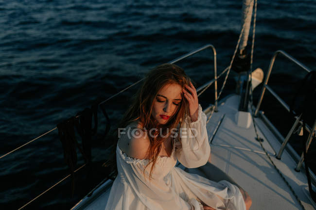 Relaxed beautiful woman sitting on bow of ship and resting while enjoying sea trip with closed eyes — Stock Photo