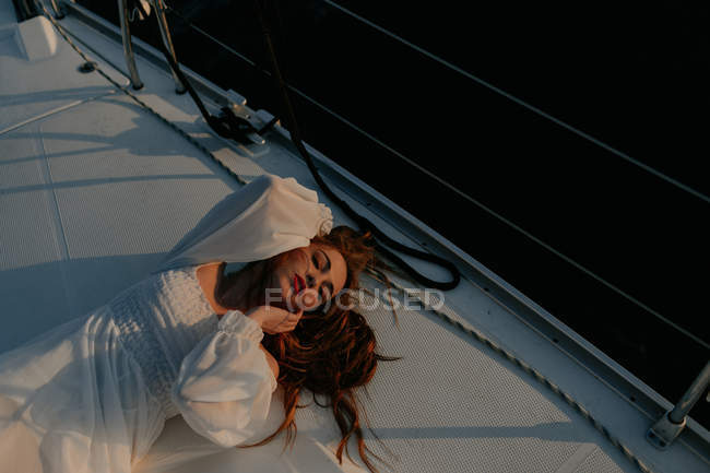 Belle femme détendue allongée sur la proue du navire et se reposant tout en profitant du voyage en mer avec les yeux fermés — Photo de stock