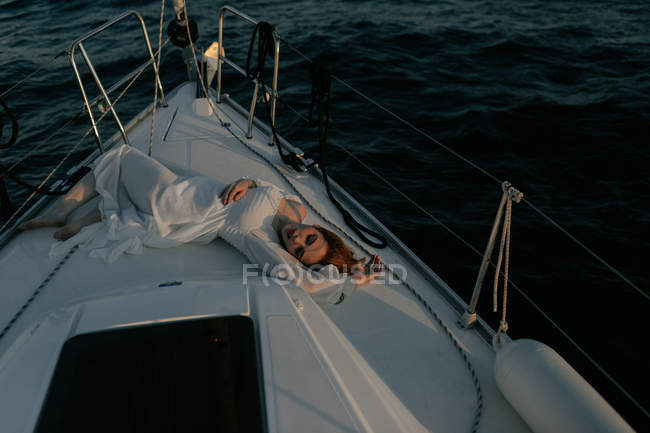 Relaxed beautiful woman lying on bow of ship and resting while enjoying sea trip with closed eyes — Stock Photo