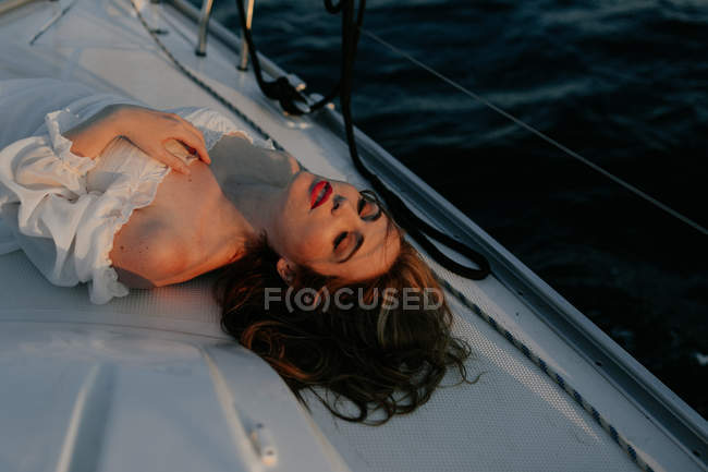 Relaxed beautiful woman lying on bow of ship and resting while enjoying sea trip with closed eyes — Stock Photo