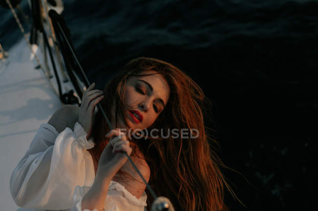 Mujer tranquila en vestido blanco de lujo descansando mientras está acostado en el yate durante el crucero con los ojos cerrados - foto de stock