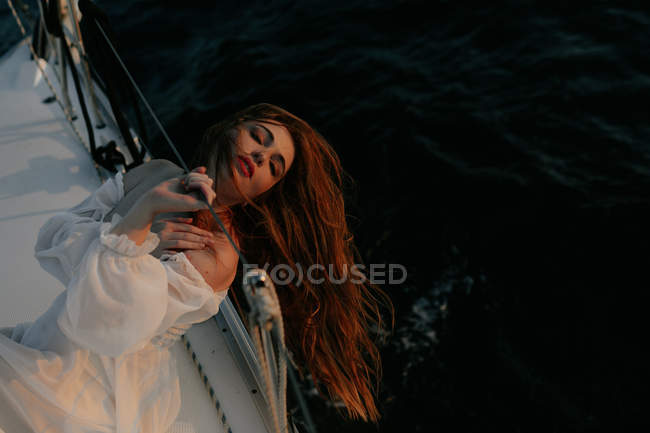 Tranquil woman in luxury white dress resting while lying on yacht during cruise with closed eyes — Stock Photo