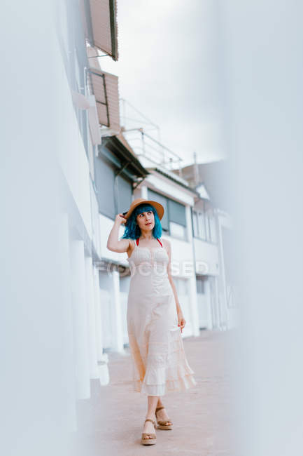 Relaxed woman with blue hair in hat and sundress strolling along city street at summer day — Stock Photo