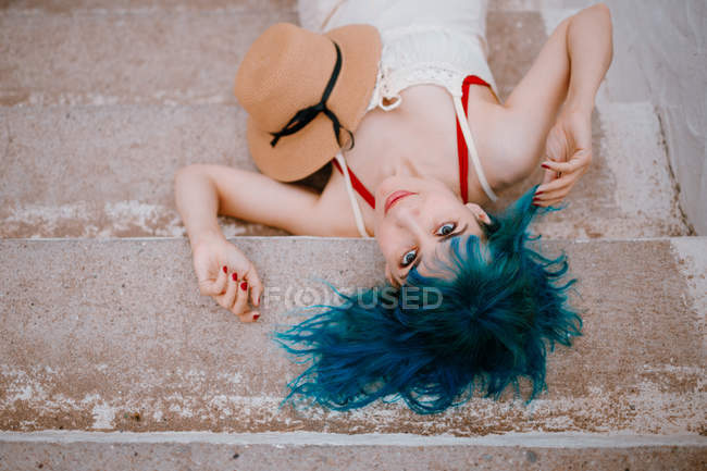 Mujer de ensueño con el pelo azul colorido en vestido de sol acostado en escalones de piedra - foto de stock