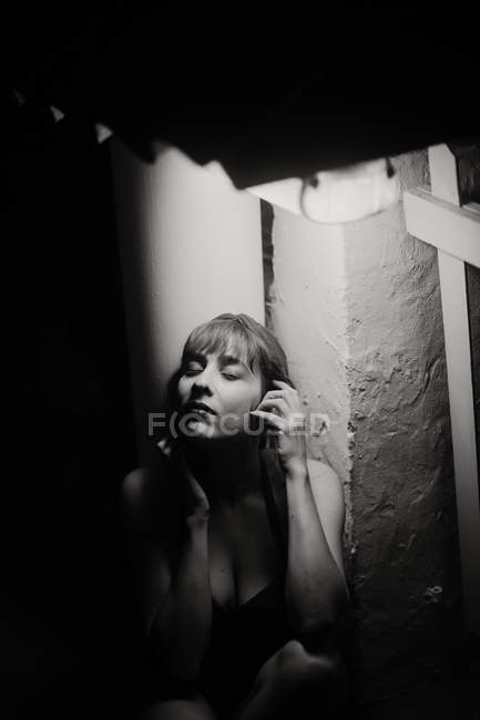 Tierna mujer apasionada con los ojos cerrados apoyados en valla de madera en la oscuridad sobre fondo negro - foto de stock