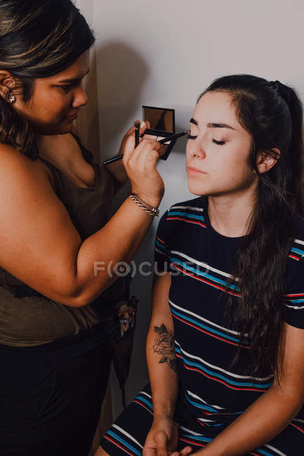 Jeune femme séduisante maquillée par une travailleuse en salon de beauté — Photo de stock