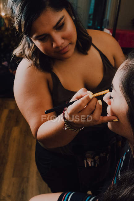Attractive young female getting makeup by professional cosmetics worker in salon — Stock Photo