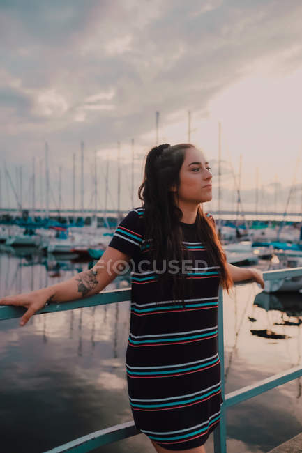 Glückliche junge tätowierte Frau im Kleid, die auf einem Kai steht, der mit Yachten und Booten gefüllt ist — Stockfoto