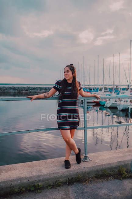 Feliz mujer tatuada joven vestida de pie sobre muelle llena de yates y barcos. - foto de stock