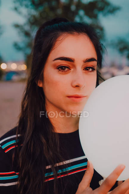 Portrait of beautiful young woman holding white light balloon while walking outdoors and looking at camera — Stock Photo