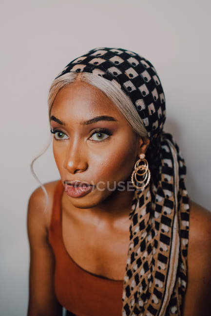 Прекрасна доросла афроамериканська жінка в коричневому вбранні з головним шарфом і сережками, дивлячись на сірий фон. — стокове фото