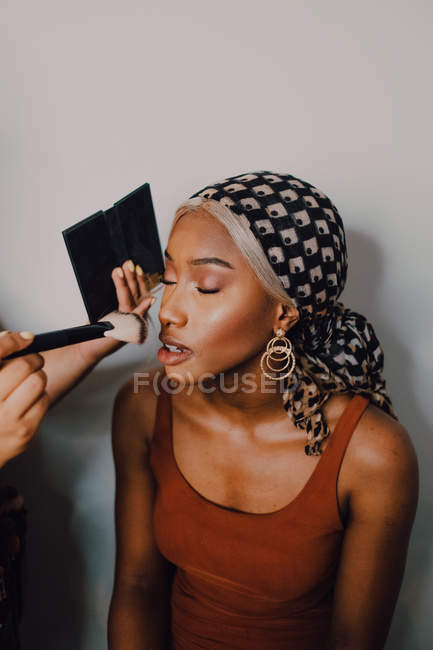 Attractive Black adult female applying eye shadow from professional makeup artist in studio — Stock Photo