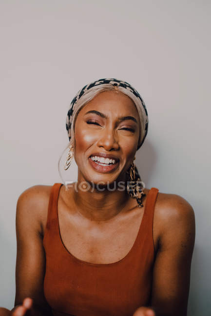 Beautiful adult African American woman in brown dress patterned headscarf and earrings looking away on grey background — Stock Photo