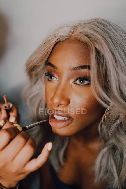Beautiful young African American woman getting lipstick on lips from professional visagiste — Stock Photo