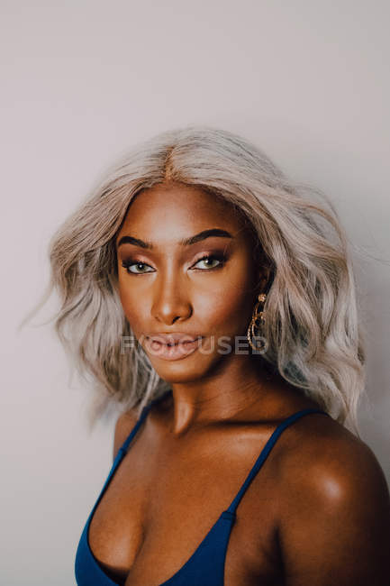 Retrato de la mujer adulta afroamericana con pelo rubio que usa azul y que mira la cámara. - foto de stock