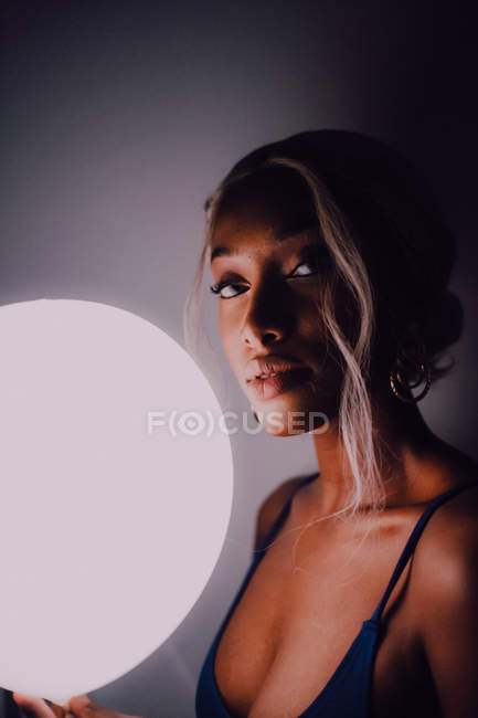 Attractive Black adult woman with white illuminated balloon in darkness looking at camera. - foto de stock
