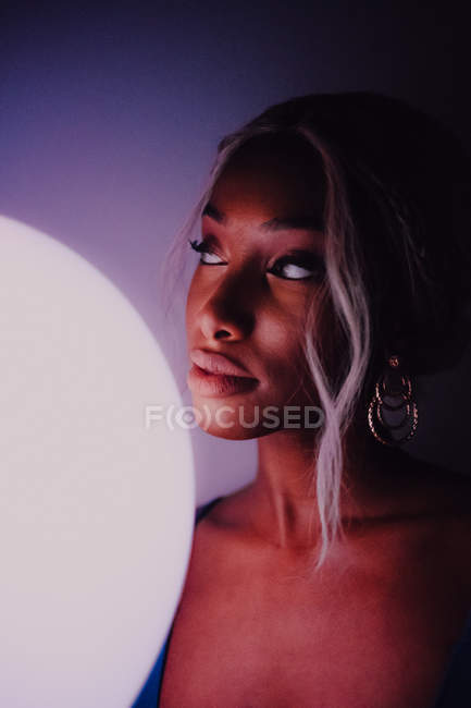 Приваблива чорна доросла жінка з білою ілюмінованою кулею в темряві дивиться на камеру — стокове фото